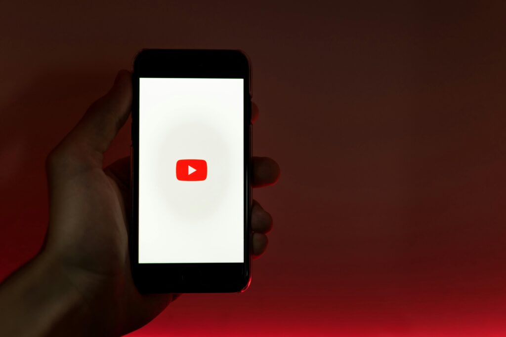 pexels-photo-3227986-3227986 A hand holding a smartphone displaying the YouTube app against a red background.