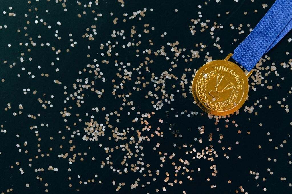 pexels-photo-6120394-6120394 Close-up of a gold medal with blue ribbon and confetti on a black surface, symbolizing victory.