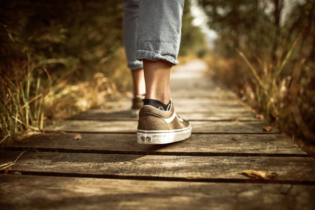 pexels-photo-631986-631986 Person wearing sneakers walking on a wooden path in a sunlit park.